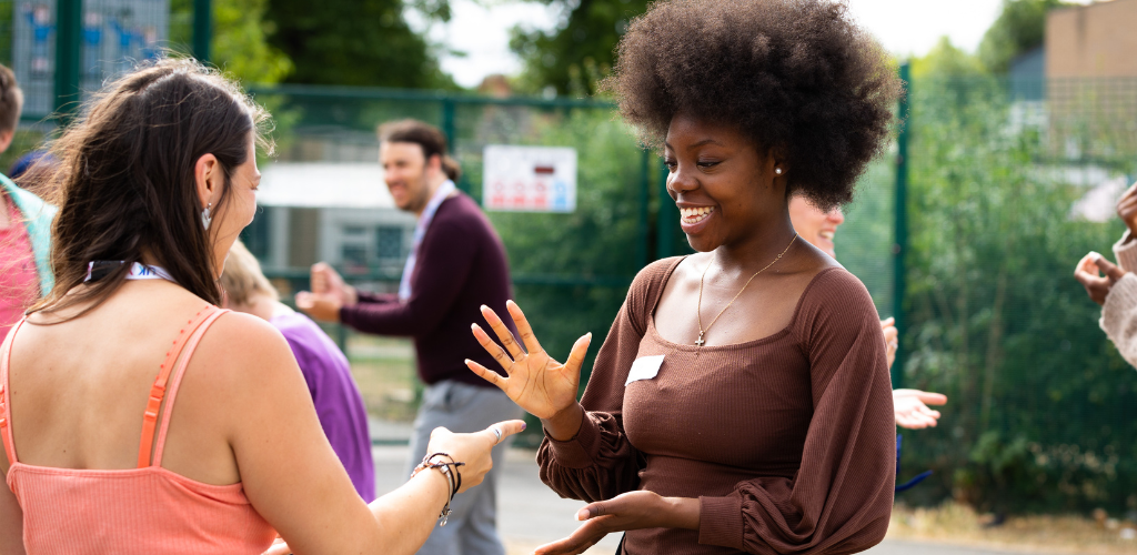 A young black woman with afro style curly hair is smiling and holding her hand out as the paper form of rock paper scissors
