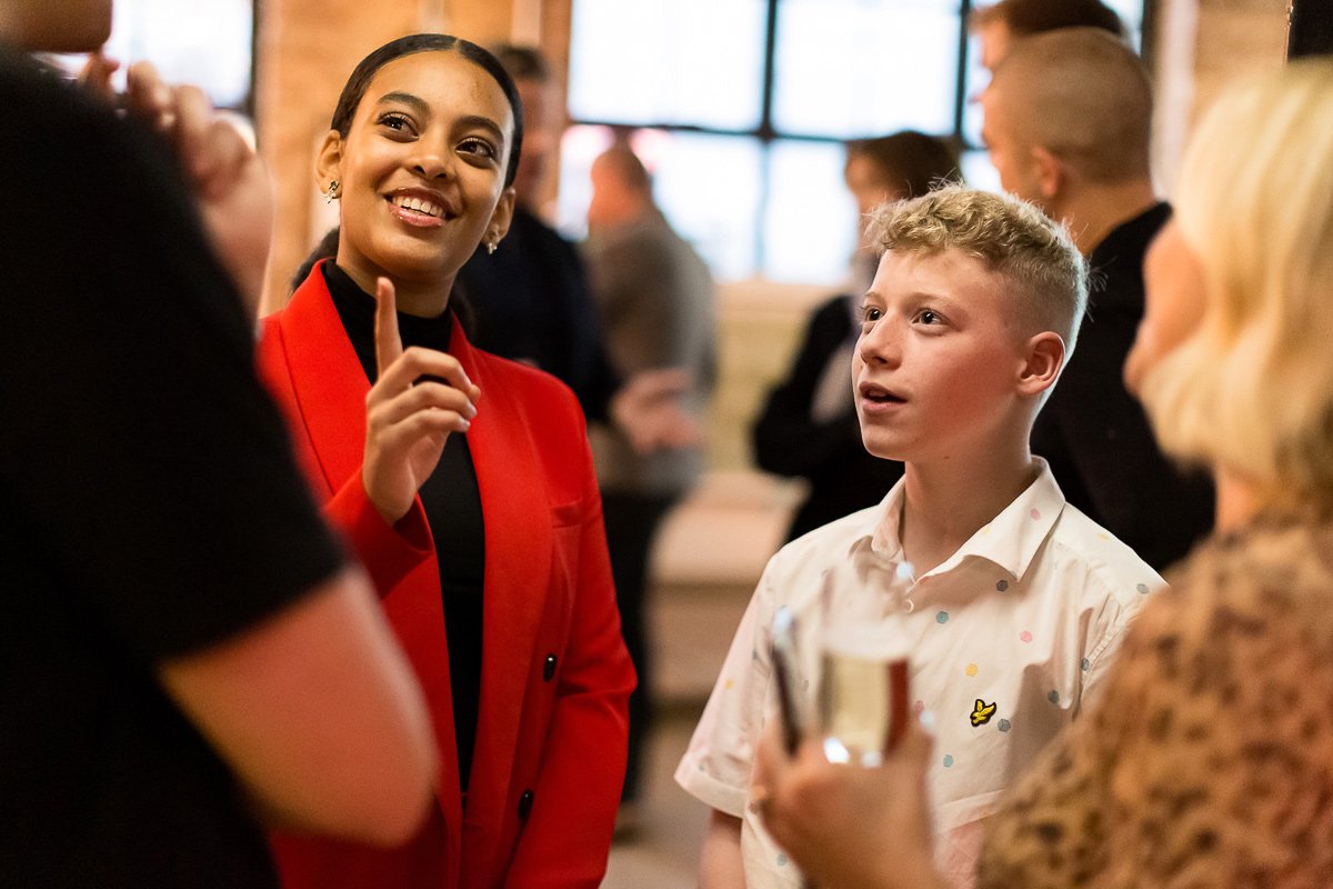Christina, a young black woman, and Jacob, a young white man, talk to a guest at Bite Back's launch event.