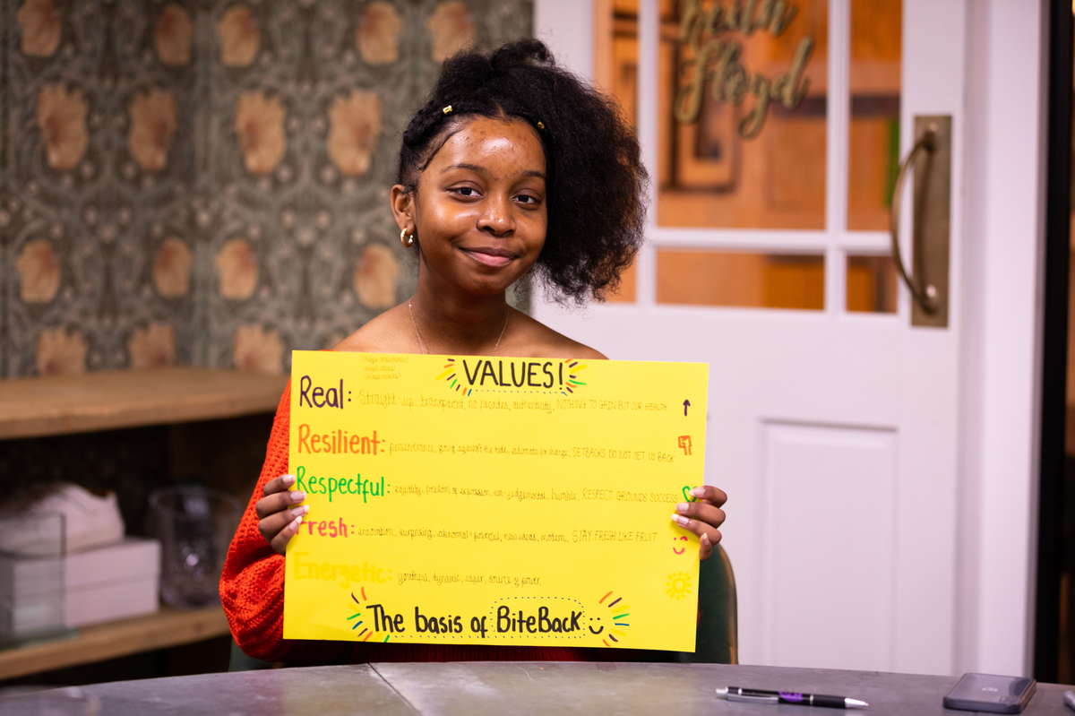 A teenage girl holding a hand drawn poster reading 'our values'.