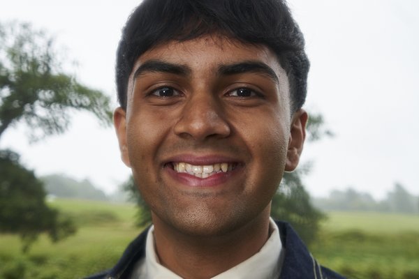 Dev is a young asian man with short straight hair. He is wearing a navy shirt and looking into the camera with a small smile on his face.