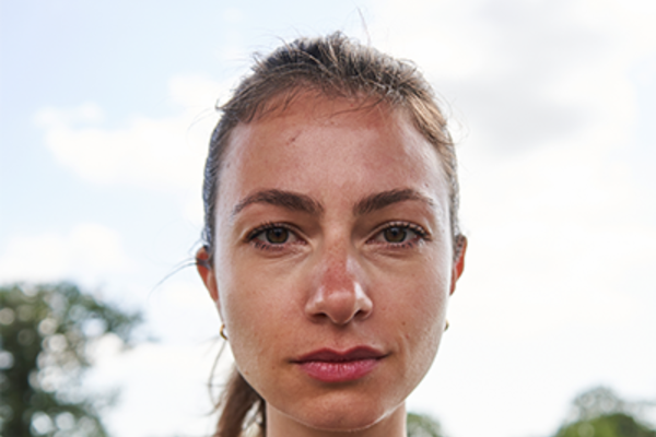 Nika is a white-skinned woman with brown hair pulled back into a sleek ponytail. She is looking straight into the camera with a fierce and serious expression, ready to bite back.