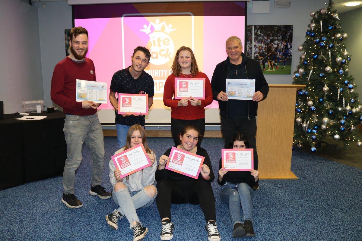 A group of CFC, a tall white man with a brown beard, a shorter man, a woman with reddish hair, an older man with grey hair, all four stood behind 3 young people sat on the floor, holding CFC certificates.
