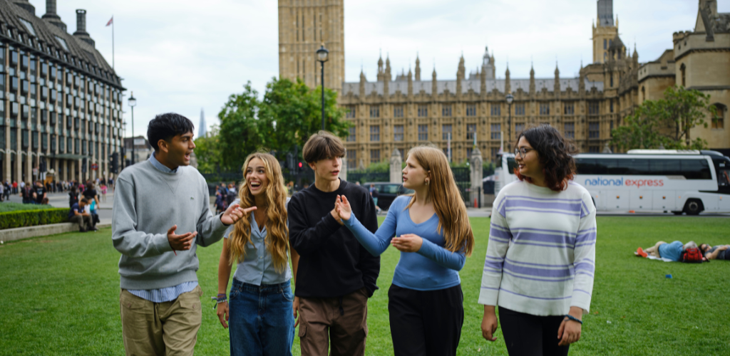 a group of young people are speaking to each other. They stand outside Westminster.