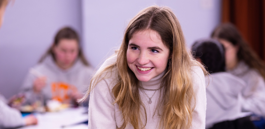 Molly is a young white woman with wavy blonde hair. She is wearing a cream jumper and smiling at the person she is speaking to.