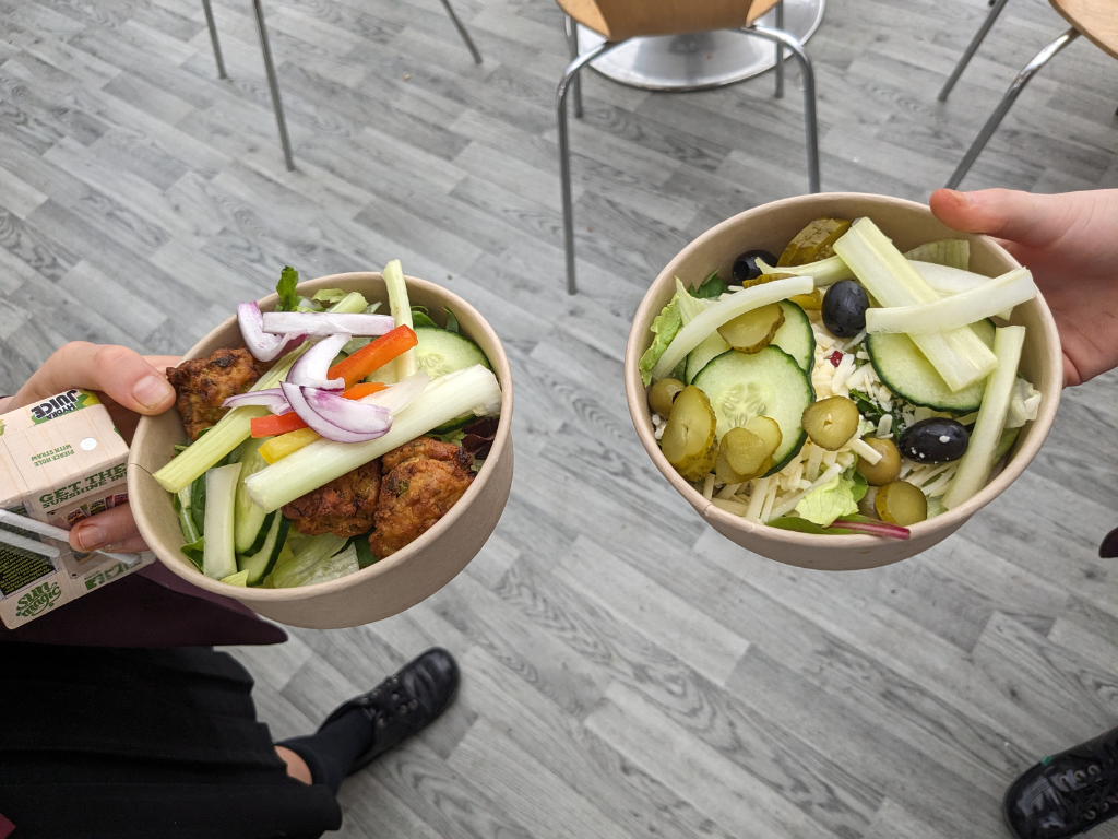 Two hands holding bowls of salad
