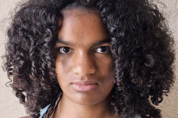 A young black woman with short curly hair is looking into the camera with a serious facial expression.